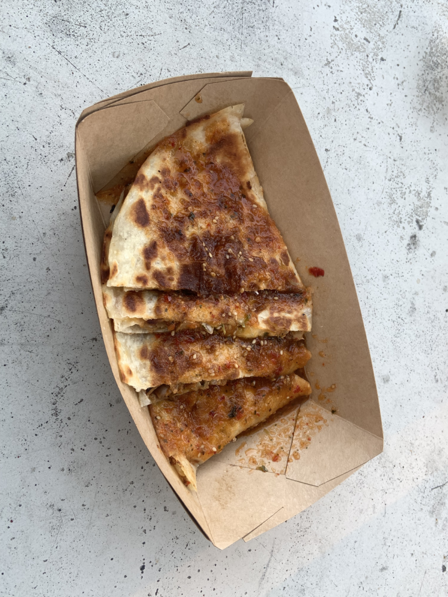 The kimchi quesadilla served on a cardboard tray doused in a layer of savory sauce.