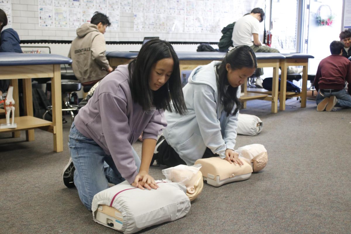 CPR certified | Medical Pathway students sophomore Mina Thongsaeng (left) and Chloe Yang practice performing CPR on a practice manikin. “I wanted to [take this class] to learn how to do CPR and learn skills such as taking vitals because it’s realistic to what you have to do in an actual hospital,” Thongsaeng said. 