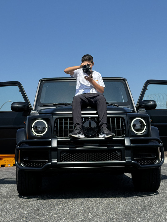 Freshman Amir Othman snaps a picture with his camera as he is seated on top of a car.