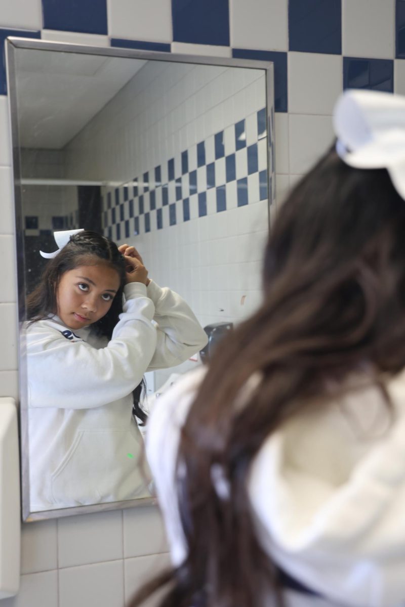 Varsity sideline cheerleader sophomore Carys Tuason adjusts her hair in preparation for an upcoming football game. “I feel [that] looking neat and looking put together is something that judges look at and other teams look at, even on game days,” Tuason said. “It is important to have our hair up because it’s also a safety thing and it can affect performance.”